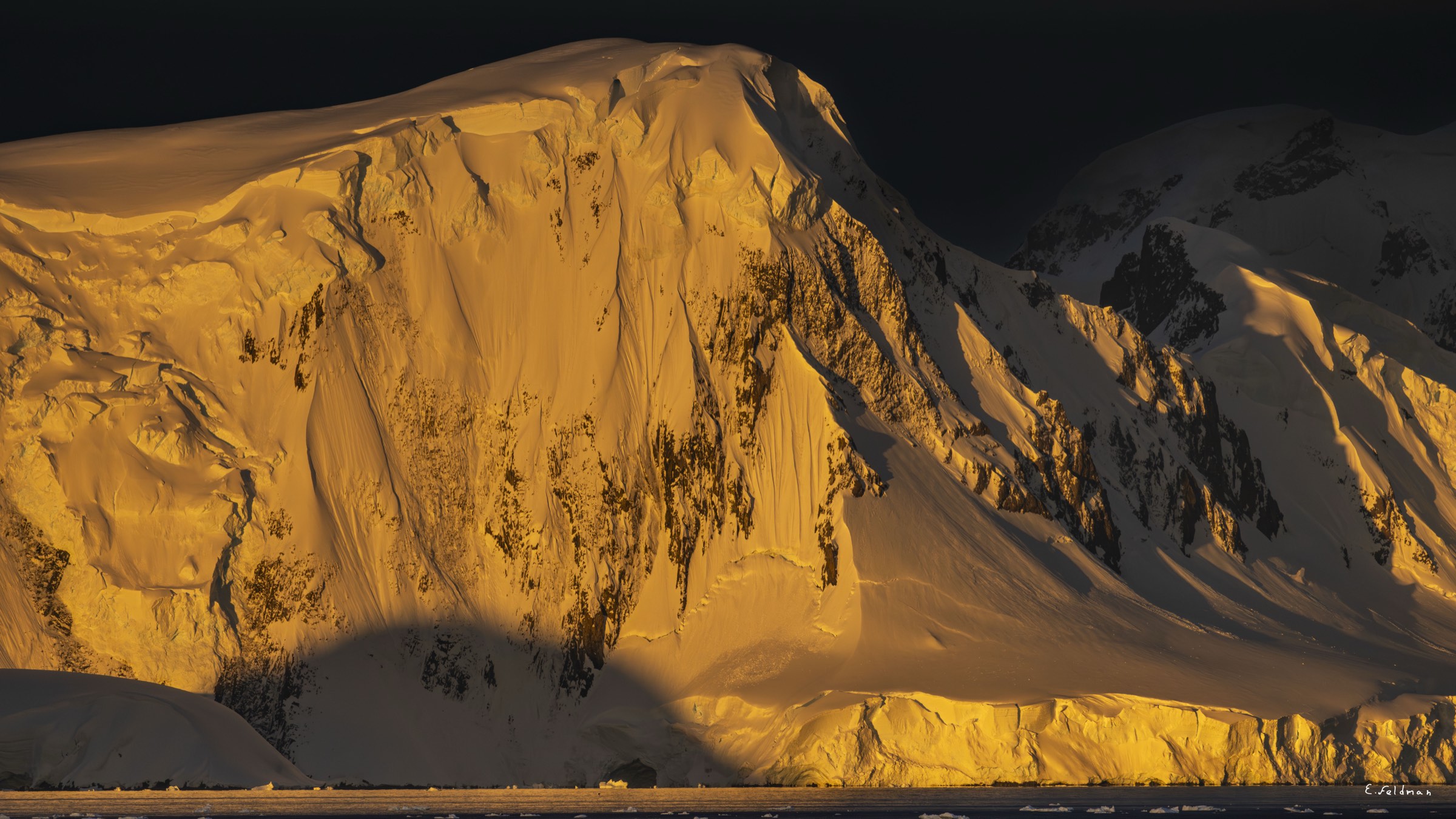 A mountain face lit gold at sunset, Antarctic Peninsula