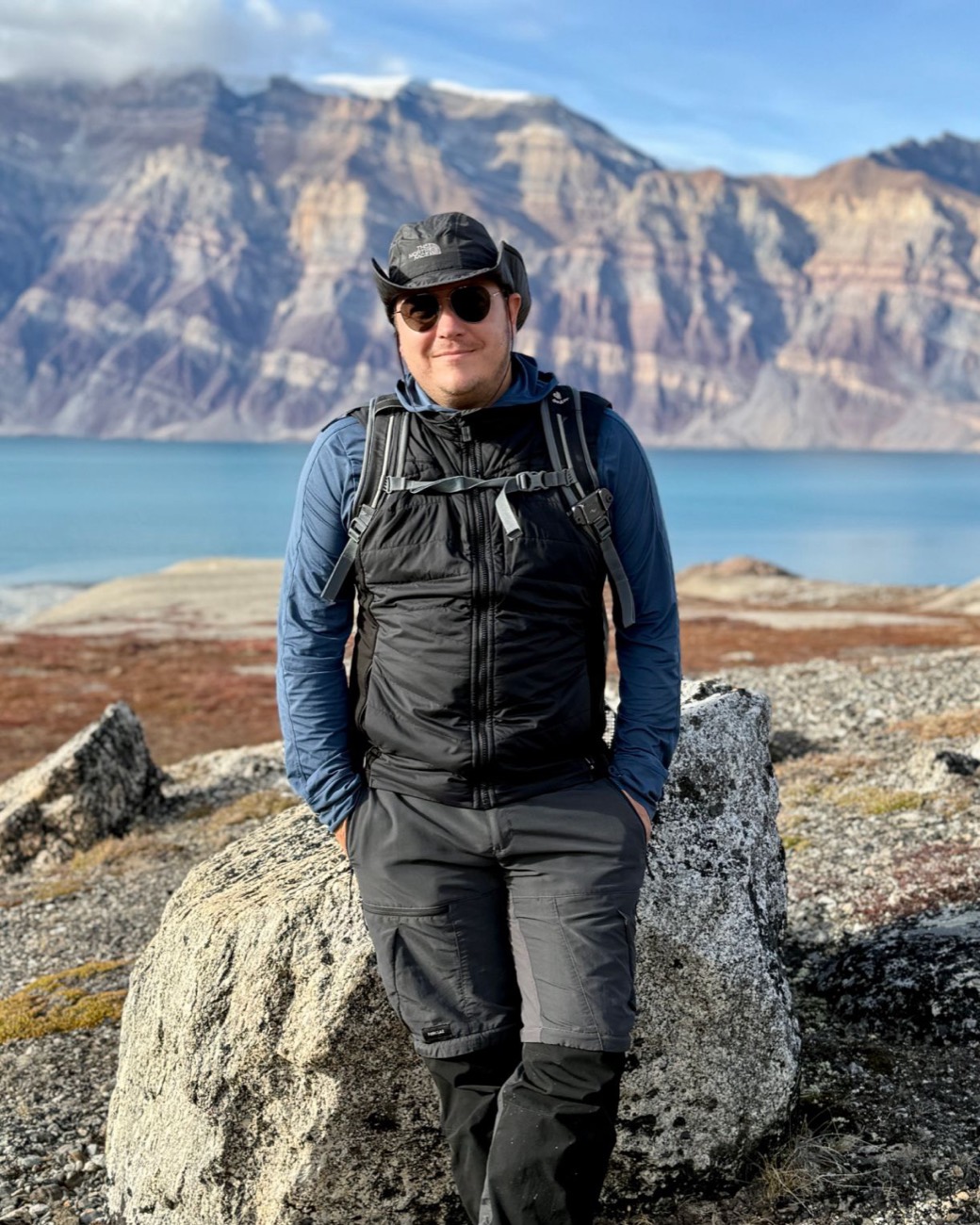 Eduardo Feldman in East Greenland, standing before a fjord and layered cliffs